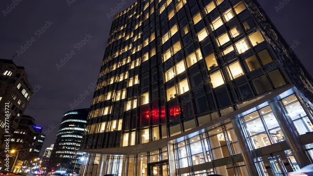 Low angle view of a modern office building at night, with lights on in many windows and a red logo displayed on the facade, suggesting ongoing activity