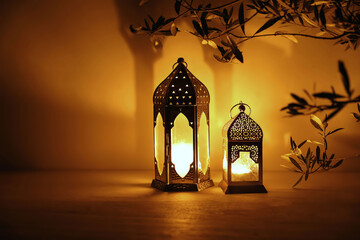 Two Moroccan lanterns on table at nigh. Blurred olive tree branches. Golden glow. Festive banner, invitation for Muslim holiday Ramadan Kareem. Eid mubarak celebration. Religion concept, copy space.