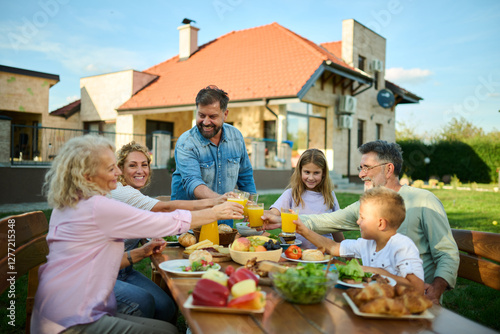 Happy extended family toasting with orange juice at backyard garden party