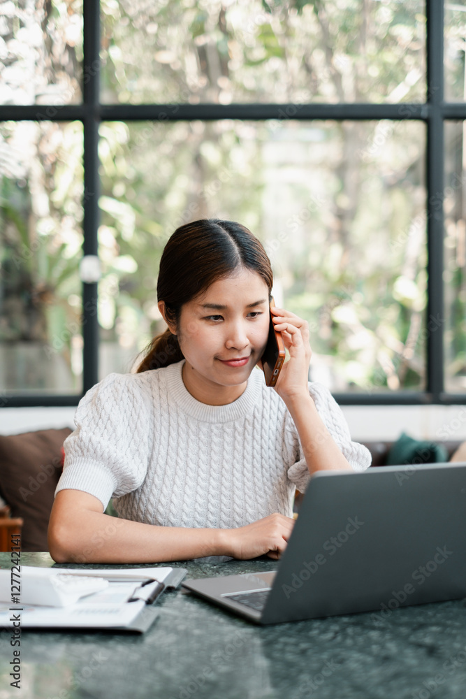 Young woman multitasking with a laptop and smartphone in a bright, modern home office setting. Young woman multitasking with a laptop and smartphone in a bright, modern home office setting.