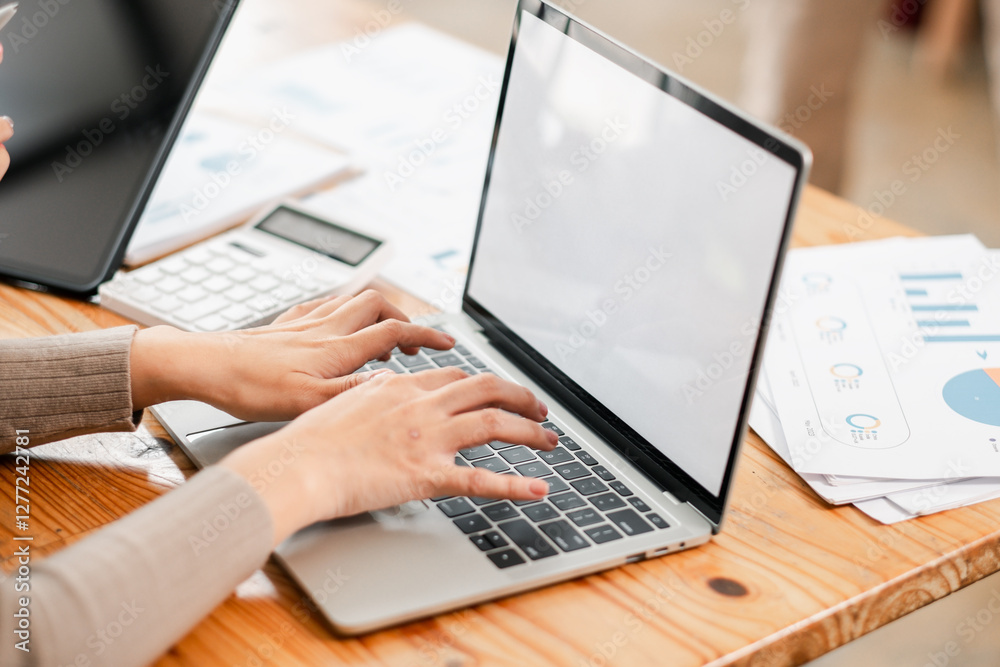 Hands typing on a laptop with financial documents and a calculator on a wooden desk, depicting a modern office environment. Hands typing on a laptop with financial documents and a calculator on a wooden desk, depicting a modern office environment.