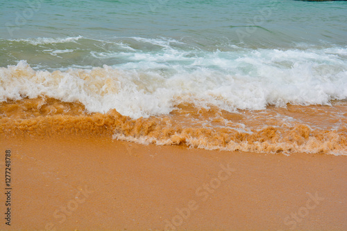 Fototapeta Naklejka Na Ścianę i Meble -  Ocean wave rolling over bright orange sand at the shoreline, creating contrast between water and beach.