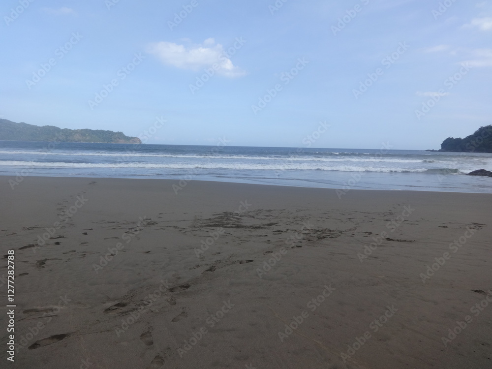 Panoramic landscape of the beach in Banyuwangi with calm waves and brown sand against a slightly cloudy blue sky background, trees in the beach Panoramic landscape of the beach in Banyuwangi with calm waves and brown sand against a slightly cloudy blue sky background, trees in the beach