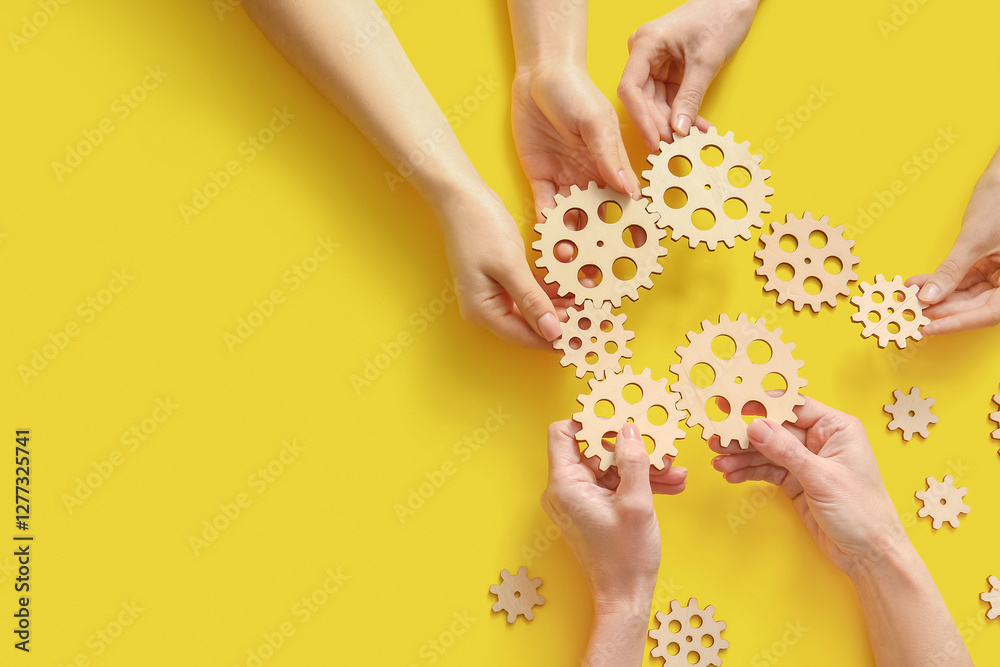 Obraz premium Hands holding wooden gears on yellow background, top view