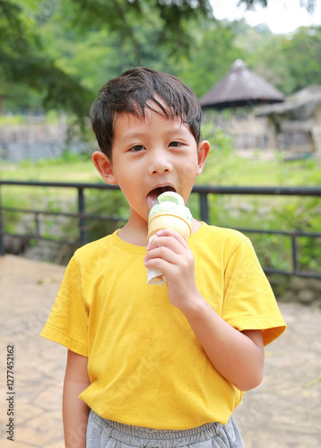 Obraz na płótnie Portrait of Asian little boy kid stands in the garden and eating ice cream. w salonie