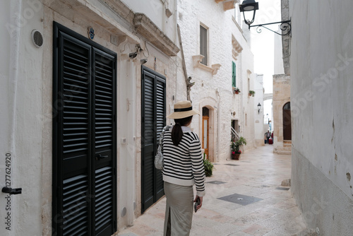 Fototapeta Naklejka Na Ścianę i Meble -  Woman among exterior architecture and decoration at 'LOCOROTONDO' historical white circular labyrinth village of narrow Italian streets- Italy