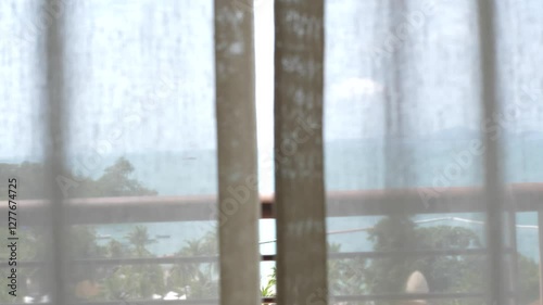Landscape view of sea through white curtain and glass window as tranquil, peaceful scene.