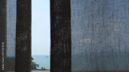 View of sea, blue sky, mountain from curtain and window as tranquil, peaceful scene.