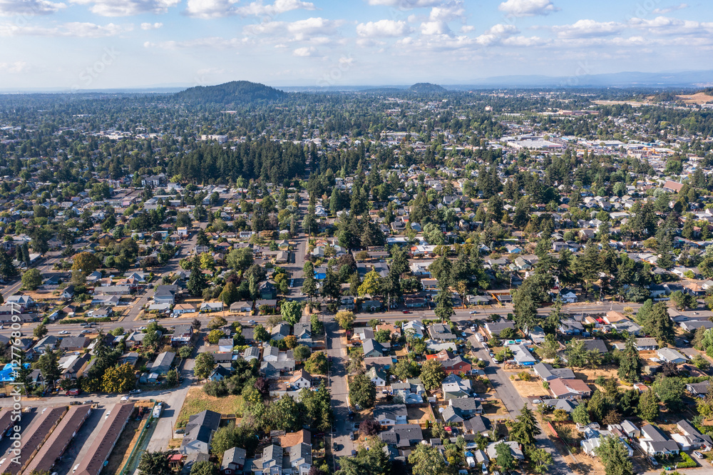 Fototapeta premium Aerial drone view of Southeast Portland, Oregon, showcasing residential neighborhoods, tree-lined streets, urban landscape, and distant downtown skyline under a partly cloudy sky