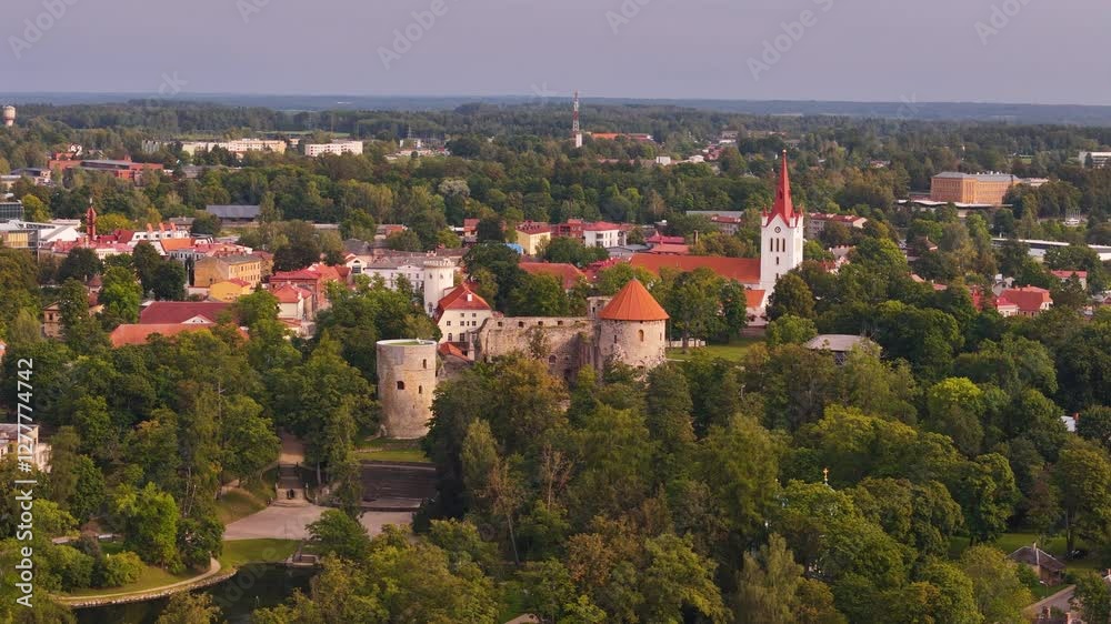 Aerial establishing left of Cesis, Latvia, showcasing a historic town center surrounded by lush greenery and slight haze in air Aerial establishing left of Cesis, Latvia, showcasing a historic town center surrounded by lush greenery and slight haze in air