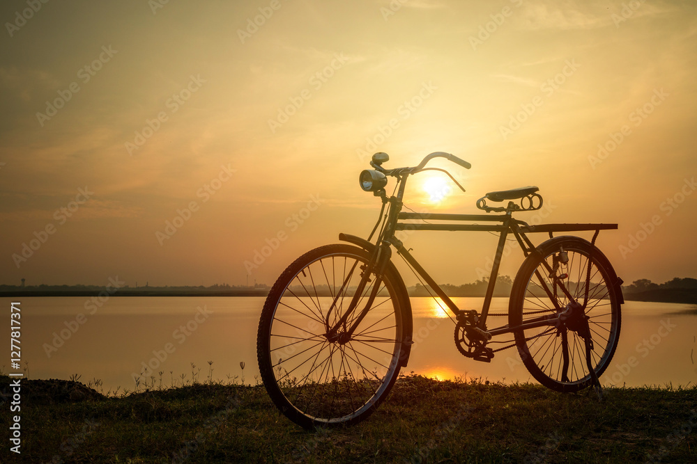 Silhouete of old rusty retro style bicycle stands in a meadow near a lake at sunset. Silhouete of old rusty retro style bicycle stands in a meadow near a lake at sunset.