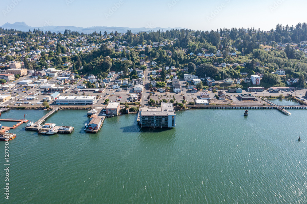 Aerial drone view of downtown Astoria, Oregon, featuring waterfront buildings, the Columbia River, a busy port, fishing boats, and lush hills in the background Aerial drone view of downtown Astoria, Oregon, featuring waterfront buildings, the Columbia River, a busy port, fishing boats, and lush hills in the background