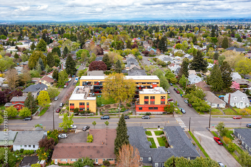 Fototapeta Naklejka Na Ścianę i Meble -  Aerial drone view of the DayBreak Cohousing building in North Portland, Oregon, surrounded by residential homes, tree-lined streets, and urban greenery on a cloudy spring day