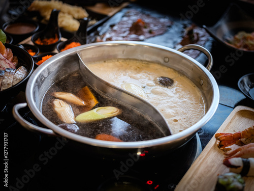Close-up photo of a stainless steel hot pot divided into two parts, with two different types of soup: a dark, rich soup on one side and a light, clear soup on the other.