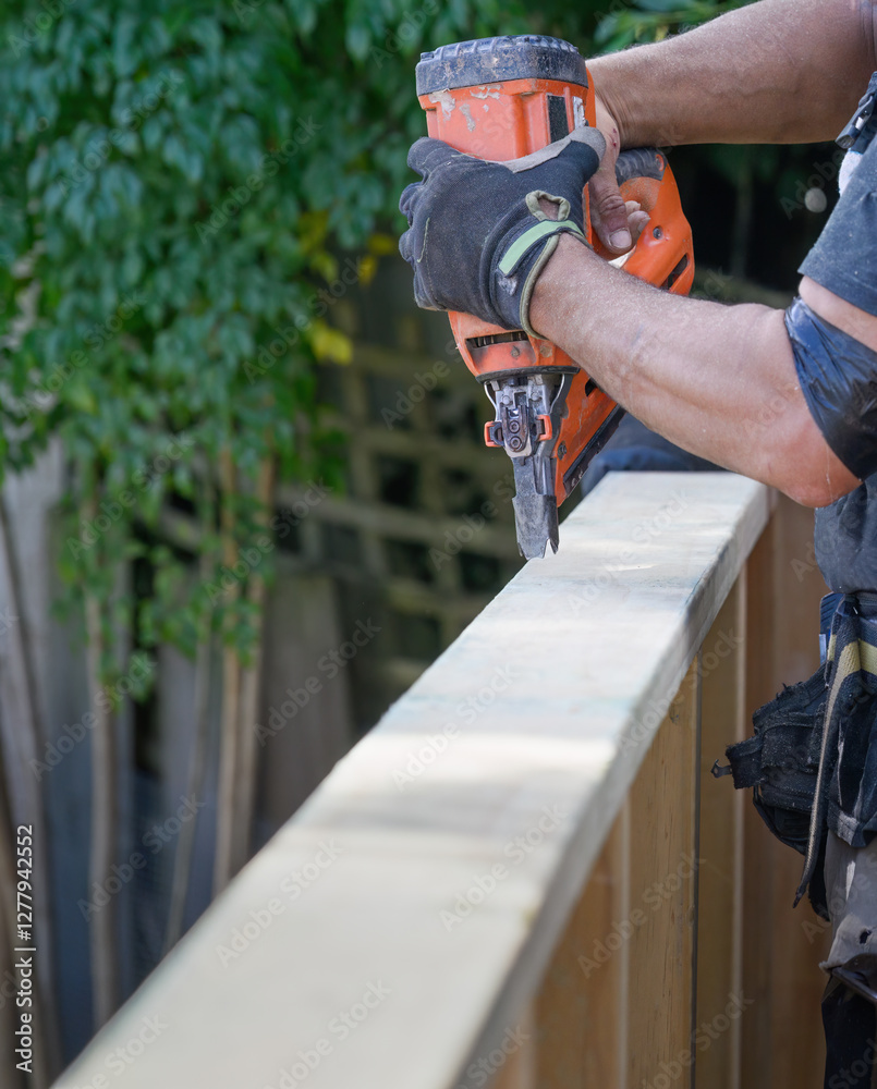 Hands of a builder working on fence using a nail gun construction tool. Vertical format.