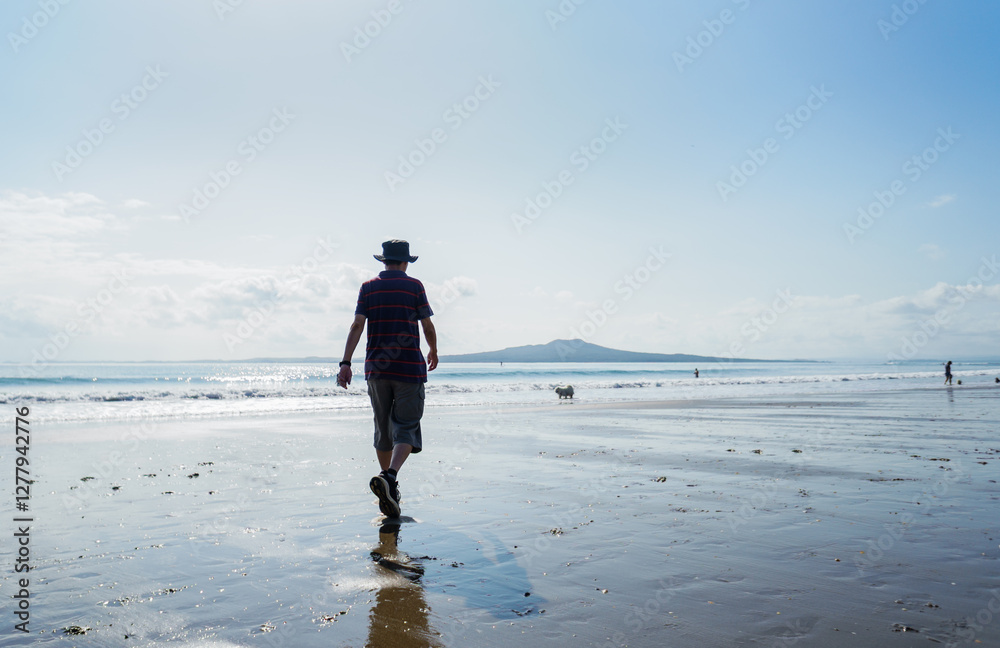 Man walking the dog on the beach. Unrecognizable people playing on Milford Beach. Auckland.