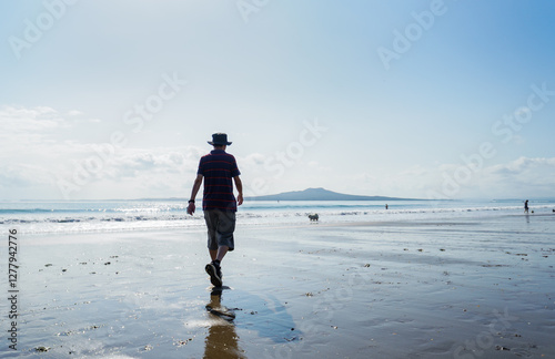 Man walking the dog on the beach. Unrecognizable people playing on Milford Beach. Auckland. photo