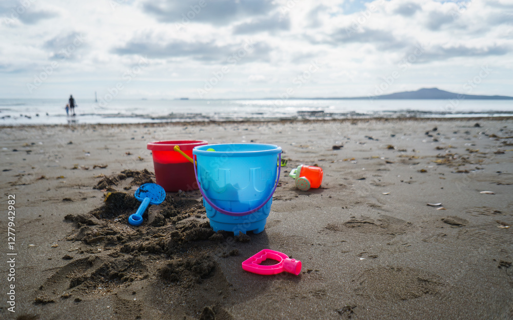 Colourful buckets and beach sand toys on the beach. Unrecognizable people playing on Milford Beach. Auckland. Colourful buckets and beach sand toys on the beach. Unrecognizable people playing on Milford Beach. Auckland.