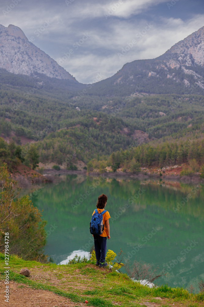 Fototapeta premium summer camp. a boy with a backpack looks at a beautiful mountain lake. trekking near a mountain lake.
