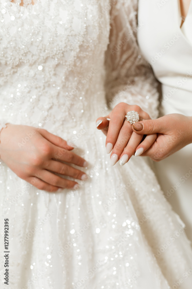 Two women hold hands. One of them is wearing a white dress with long lace sleeves, decorated with sequins. Two women hold hands. One of them is wearing a white dress with long lace sleeves, decorated with sequins.