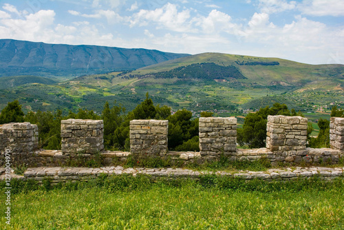 A view from the fortified walls of the 13th century Berat Castle in Albania. A picturesque rural landscape of pine trees, fields and green hills, with the Shpirag Mountain Range left