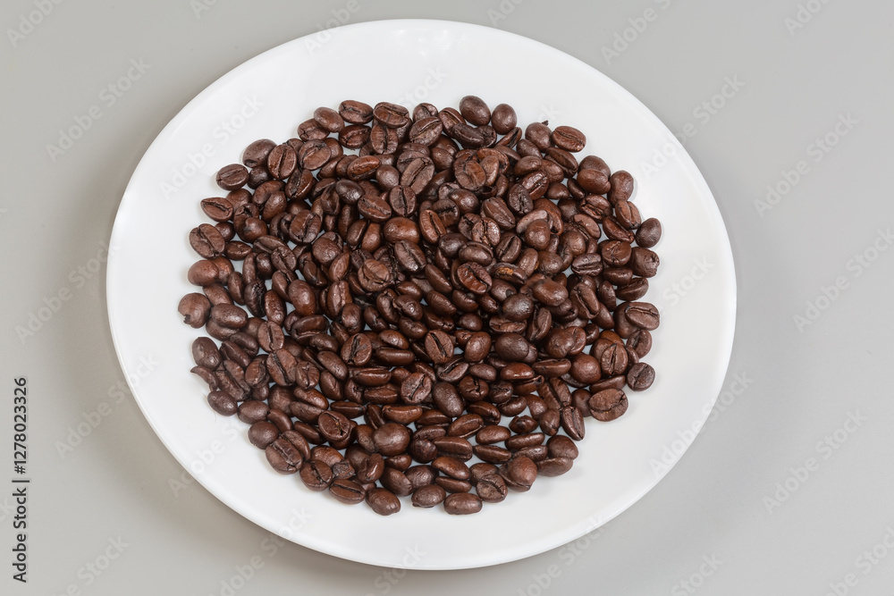 Dark roasted coffee beans on white dish on gray background