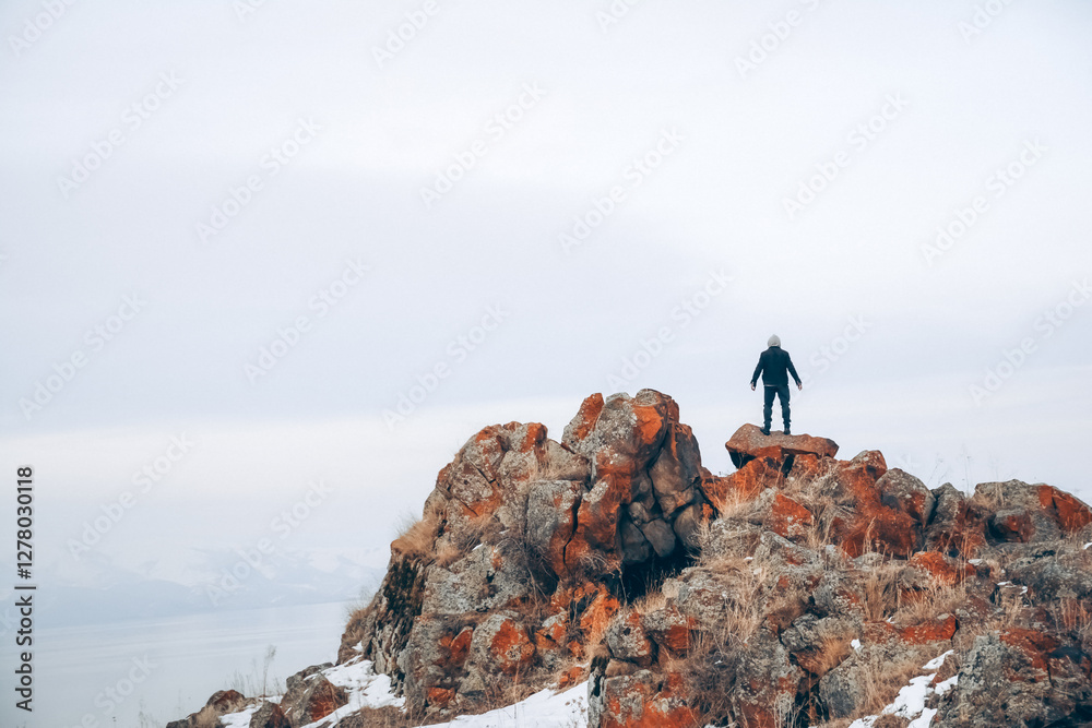 Fototapeta premium A man stands on the top of a cliff. A traveler stands on the top of a mountain and looks at the sea. Beautiful documentary landscape. Beautiful nature with a rocky mountain and a lake