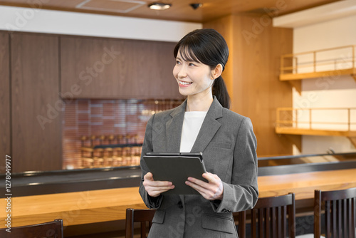 タブレットを持って店内を見るスーツを着た女性 photo