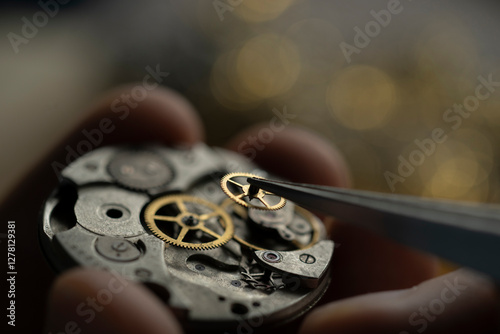 Man's hands repairing old watch, holding a part with tweezer.
