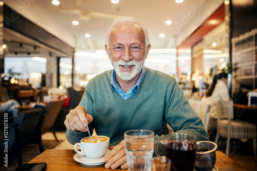 Portrait of senior man stirring coffee in coffee shop and smiling at camera.
