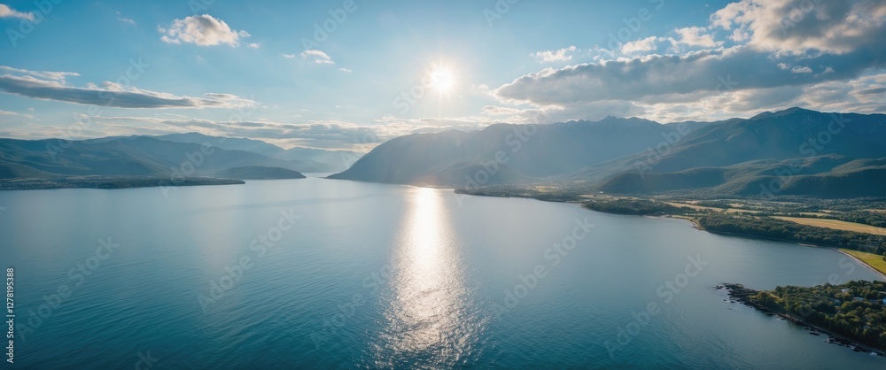 Aerial view of a tranquil lake surrounded by mountains under a bright sunlit sky with scattered clouds and a reflective water surface Aerial view of a tranquil lake surrounded by mountains under a bright sunlit sky with scattered clouds and a reflective water surface