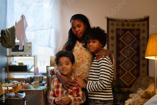 Portrait of African American mother hugging two children inside warmly lit living room with home decorations and family belongings