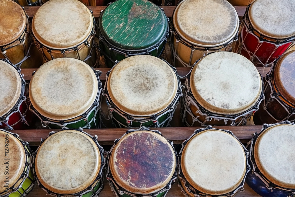 Collection of world percussion instruments displayed on wooden rack showcasing diverse designs and materials Collection of world percussion instruments displayed on wooden rack showcasing diverse designs and materials