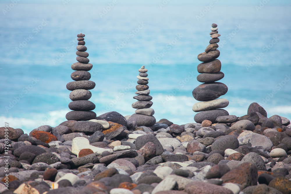 Stone towers stand tall, testament to precision and patience required to achieve equilibrium on rocky shore. Stacks of balanced stones of varying heights on rocky beach with the ocean in background