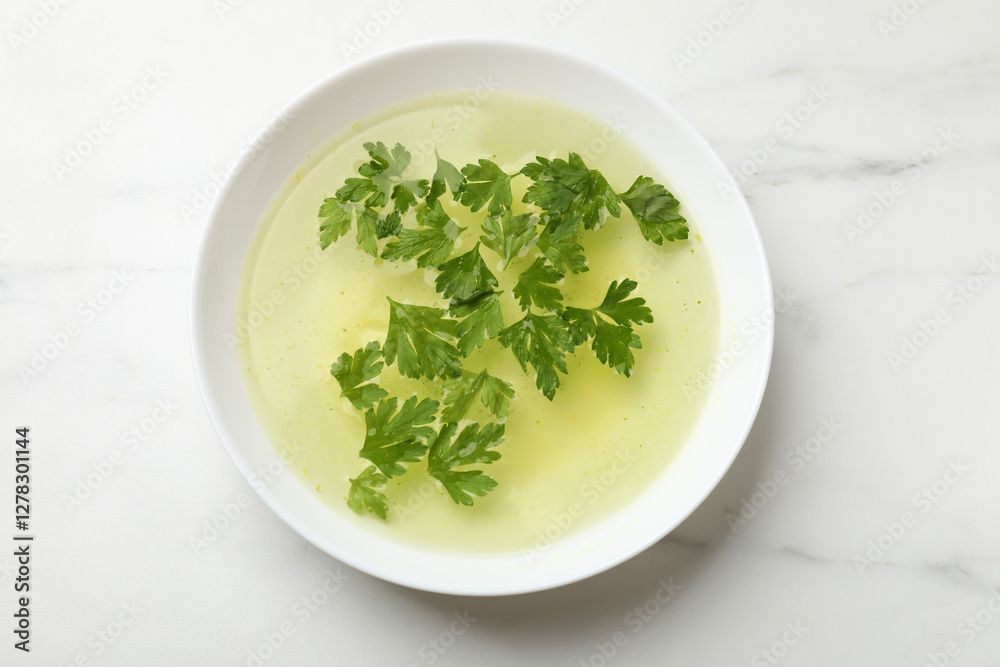 Tasty chicken bouillon in bowl on white marble table, top view Tasty chicken bouillon in bowl on white marble table, top view