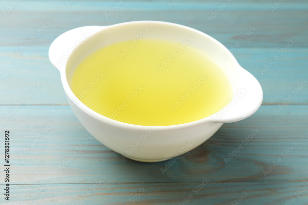 Tasty chicken bouillon in bowl on light blue wooden table, closeup Tasty chicken bouillon in bowl on light blue wooden table, closeup