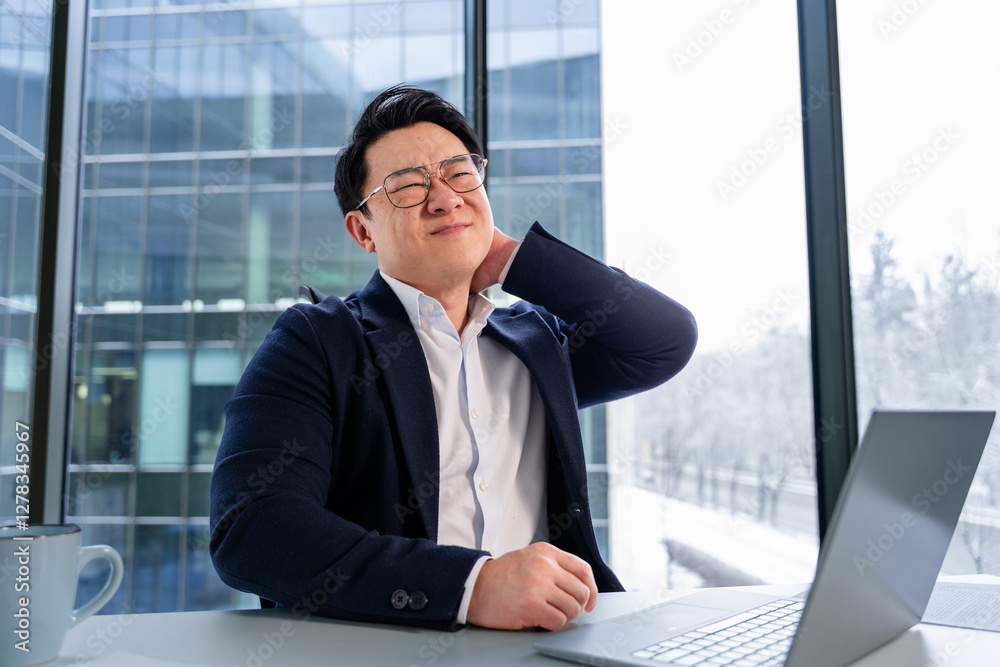 Professional Asian businessman in an office setting, showing physical discomfort during tasks, wearing business attire at a desk with a laptop and a window view of modern architecture. Professional Asian businessman in an office setting, showing physical discomfort during tasks, wearing business attire at a desk with a laptop and a window view of modern architecture.