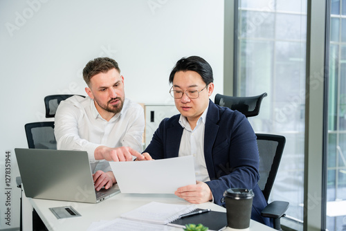 Coworkers analyzing a document together at a modern workplace, fostering teamwork and professional collaboration. Focused atmosphere, business attire adds to the sense of refined professionalism.