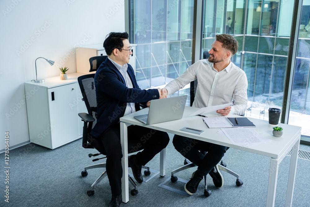 Two professional businessmen shaking hands at a desk in a modern office, signifying agreement, collaboration, and success amidst a bright and productive setting. Two professional businessmen shaking hands at a desk in a modern office, signifying agreement, collaboration, and success amidst a bright and productive setting.