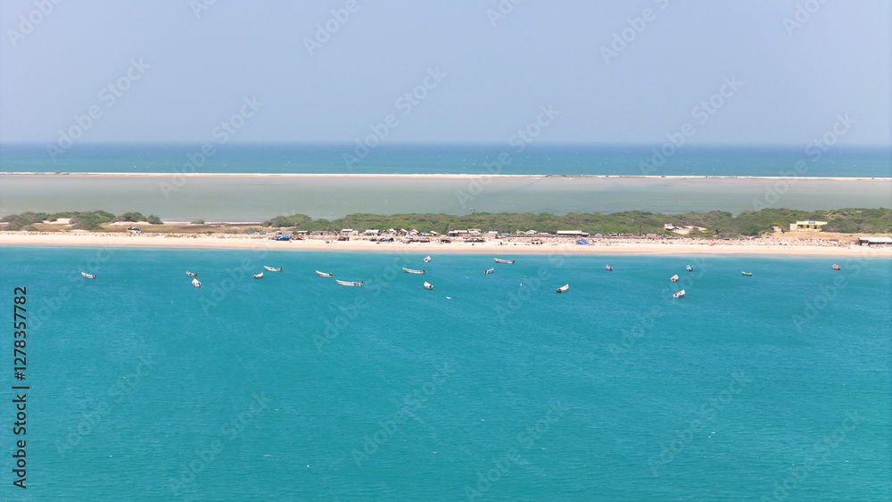 Fototapeta premium Aerial view of Dhanushkodi’s famous road cutting through the Indian Ocean, with fishing boats scattered along the coastline. with small houses