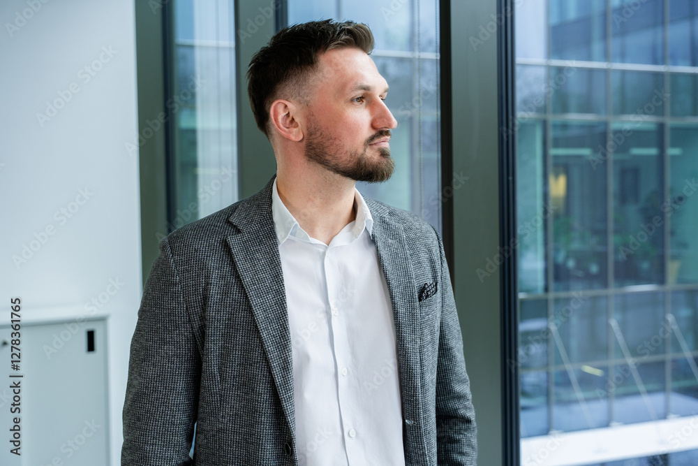 Professional businessman in a sharp suit poses confidently near a large glass window of a contemporary office building, evoking a sense of ambition and success. Professional businessman in a sharp suit poses confidently near a large glass window of a contemporary office building, evoking a sense of ambition and success.
