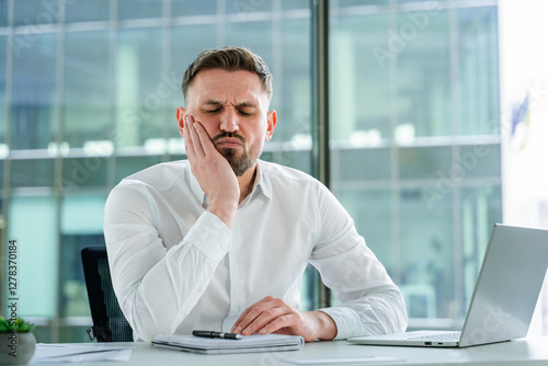 Professional businessman experiencing pain at a modern office desk, portraying discomfort and frustration. Formal shirt attire enhances the professional environment's authenticity.