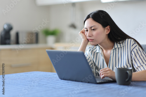 Bored asian woman checking laptop in a kitchen