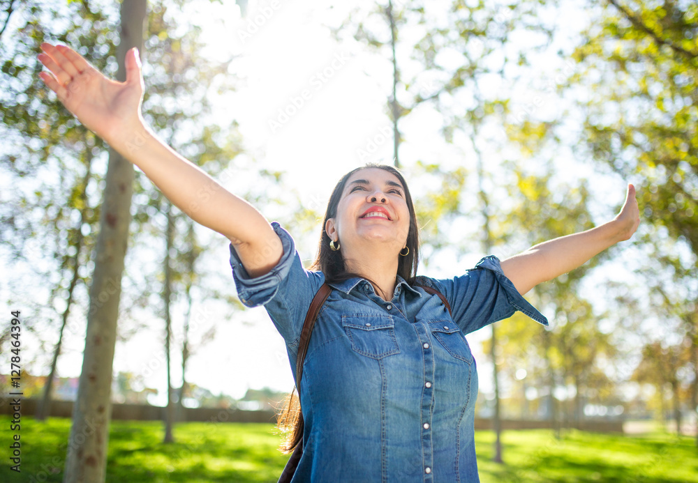 Happy woman in casual denim shirt with arms raised enjoying nature in a park Happy woman in casual denim shirt with arms raised enjoying nature in a park