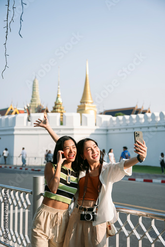 Canvas Print Two happy tourists taking selfie in bangkok with grand palace in background