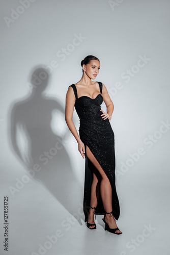 Elegant portrait of a brunette girl in a black dress with sequins under the light of lamps in the studio. Luxury fashion collection of dresses