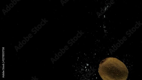 Slow motion one kiwi spinning falling into transparent water on black background. Fresh fruit splashing in aquarium. Healthy food, diet, air bubbles