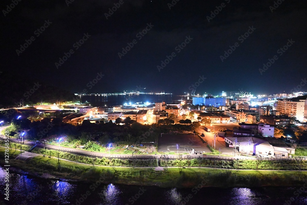Naklejka premium Coastal City Nightscape with Illuminated Port and Reflections