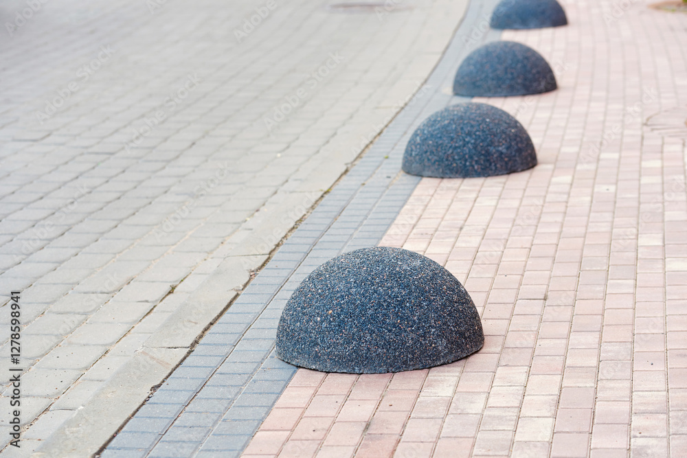 Dome shaped bollards installed along the sidewalk as an anti-parking measure, providing pedestrian safety and preventing unauthorized vehicle access in urban areas. Bollards in row closeup