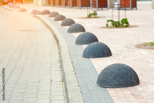Anti-parking dome bollards placed in row on the sidewalk to restrict vehicle access and ensure pedestrian safety in well planned urban environment. Bollards on the sidewalk, traffic control measure
